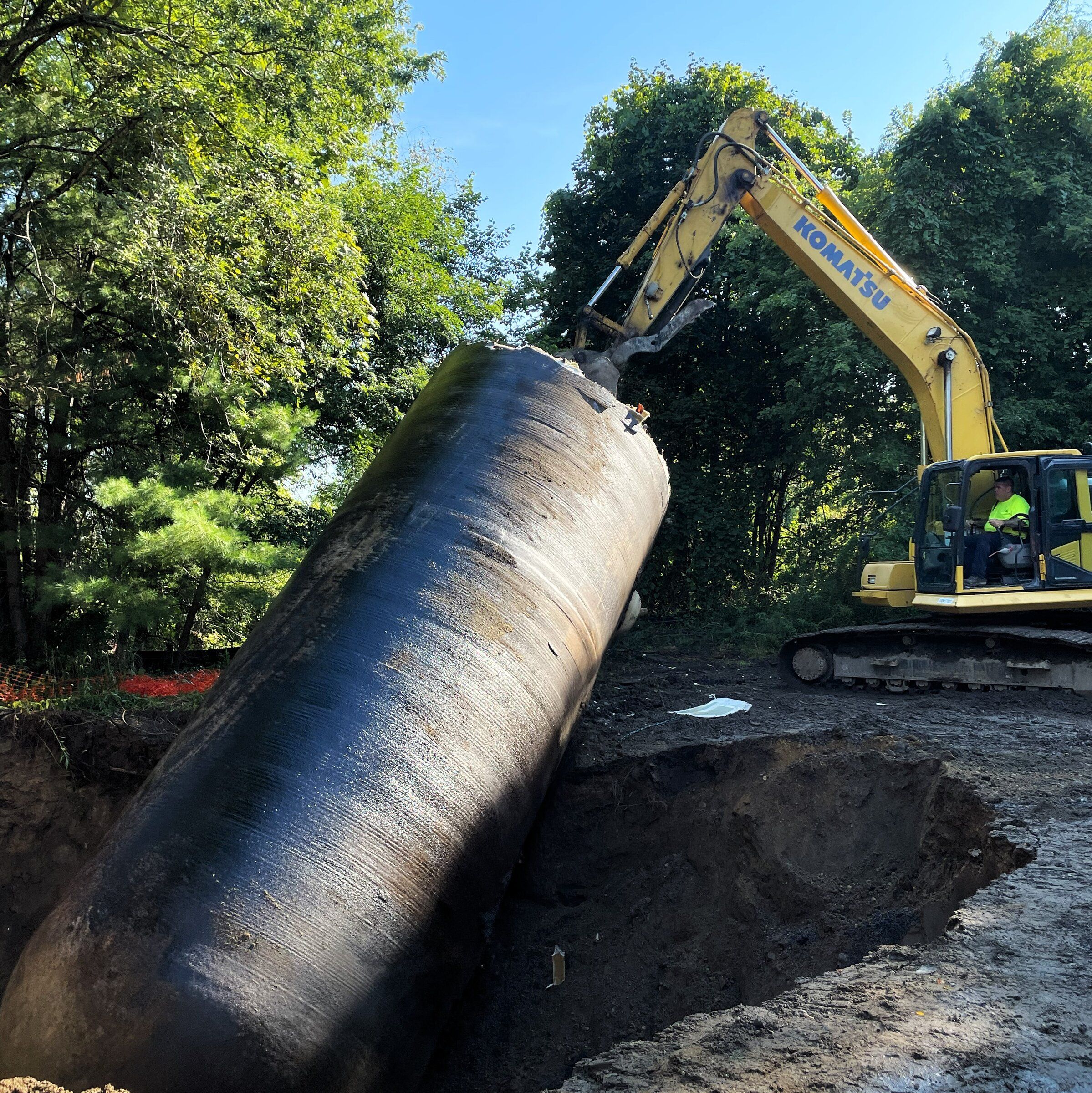 Excavator lifting a large black underground fuel oil tank out of the ground