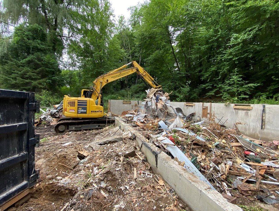Excavator loading demolition debris into a roll-off container