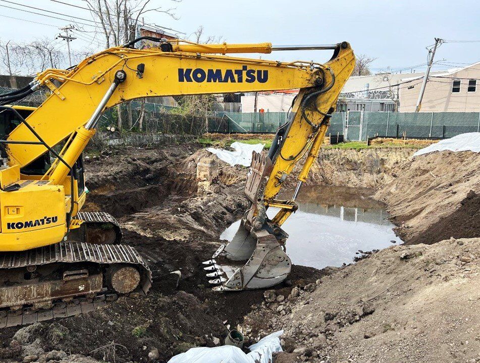 Komatsu excavator digging in a wet excavation with stockpiles behind it