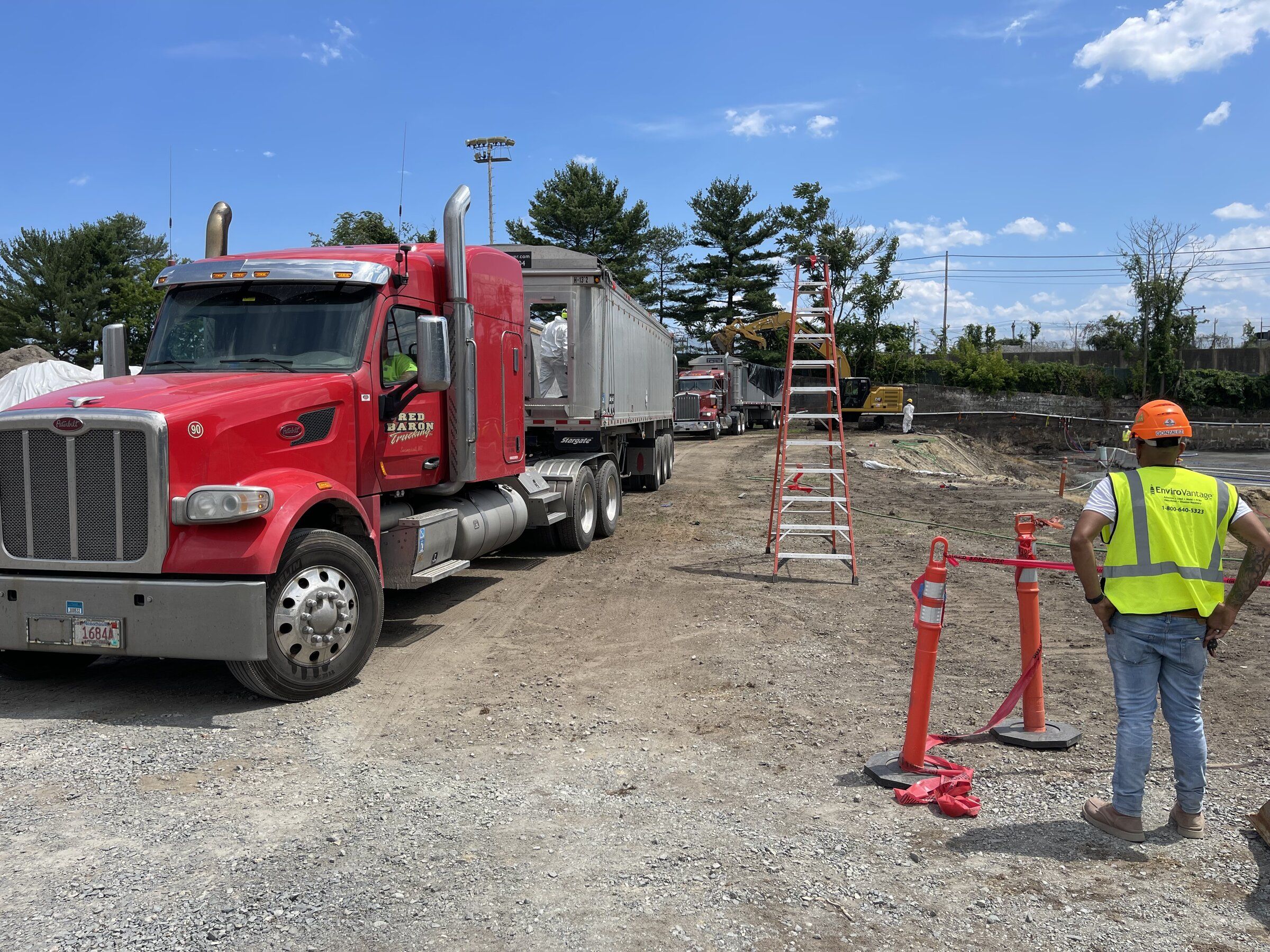 Tractor-trailer dump truck staged on site while a crew member in a safety vest directs loading