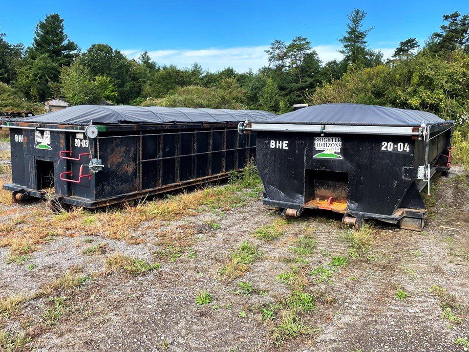 Two covered roll-off containers staged on a gravel lot