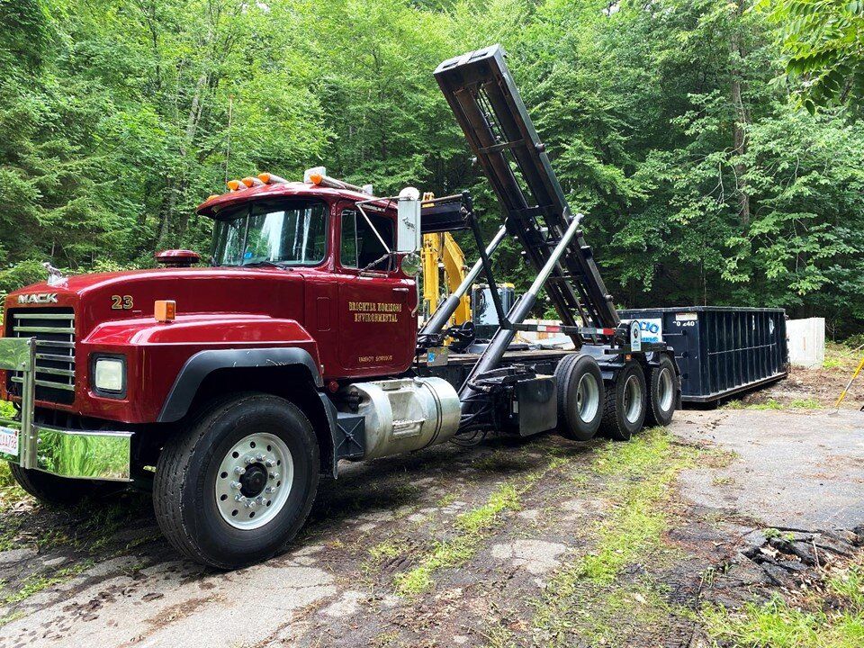 Red roll-off truck carrying a container on a gravel lot