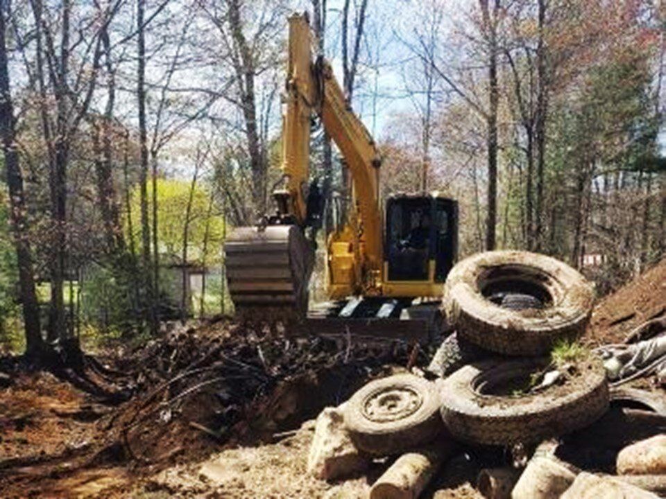 Excavator clearing old tires and debris from a wooded lot