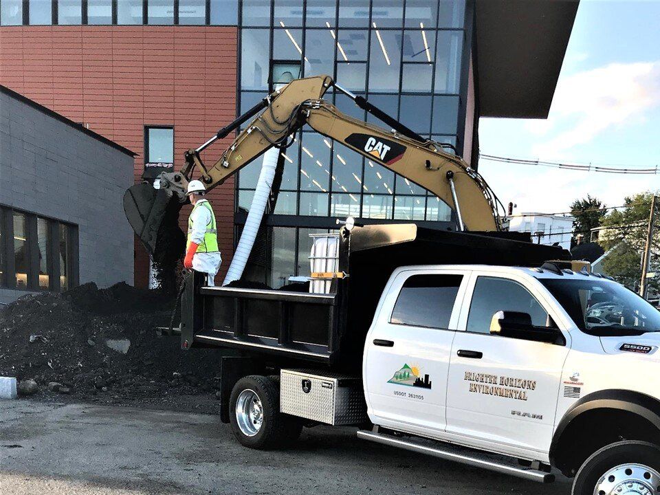 CAT excavator loading soil into a pickup dump truck outside a modern building