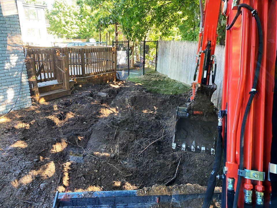 Excavator bucket working soil in an excavation beside a house