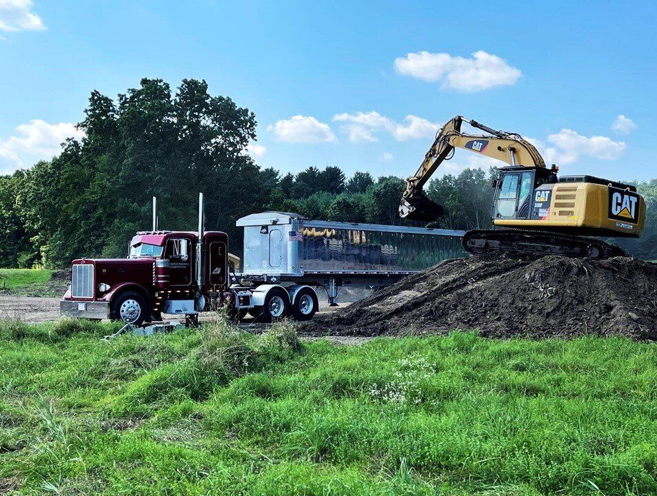 CAT excavator loading a red tractor-trailer dump truck in a grassy field